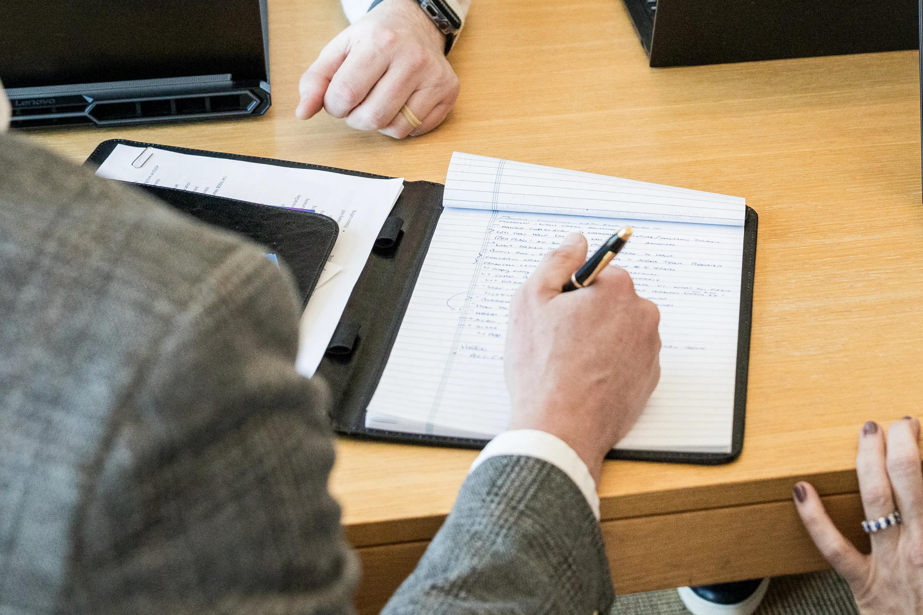 Close-up of a person taking handwritten notes on a legal pad during a meeting
